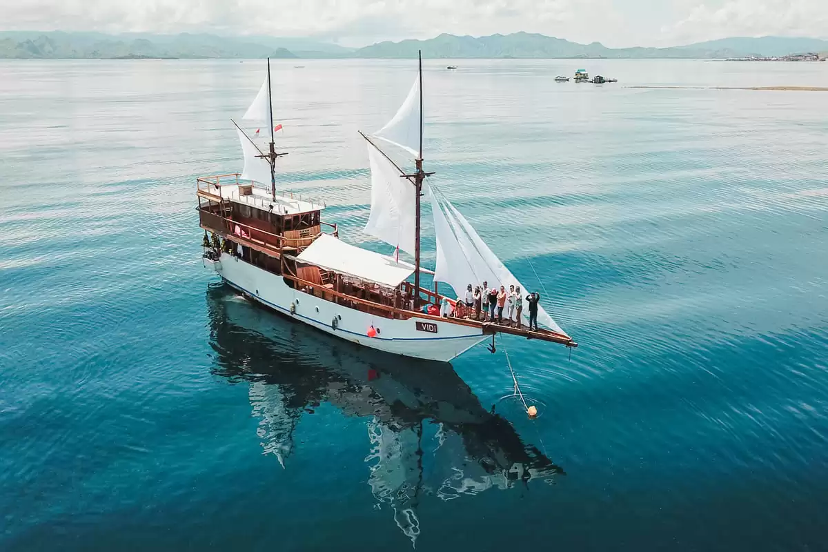 A phinisi under sail seen from the air with guests on the bowsprit