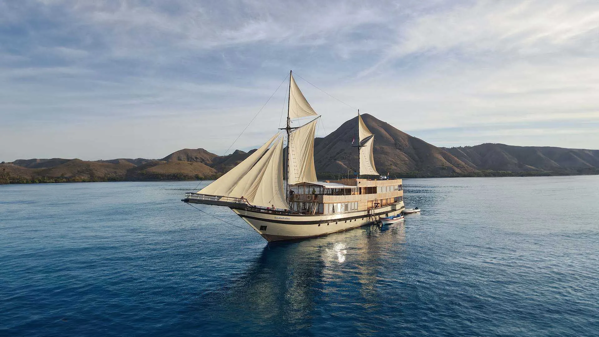 A phinisi under full sail in Komodo waters at golden hour