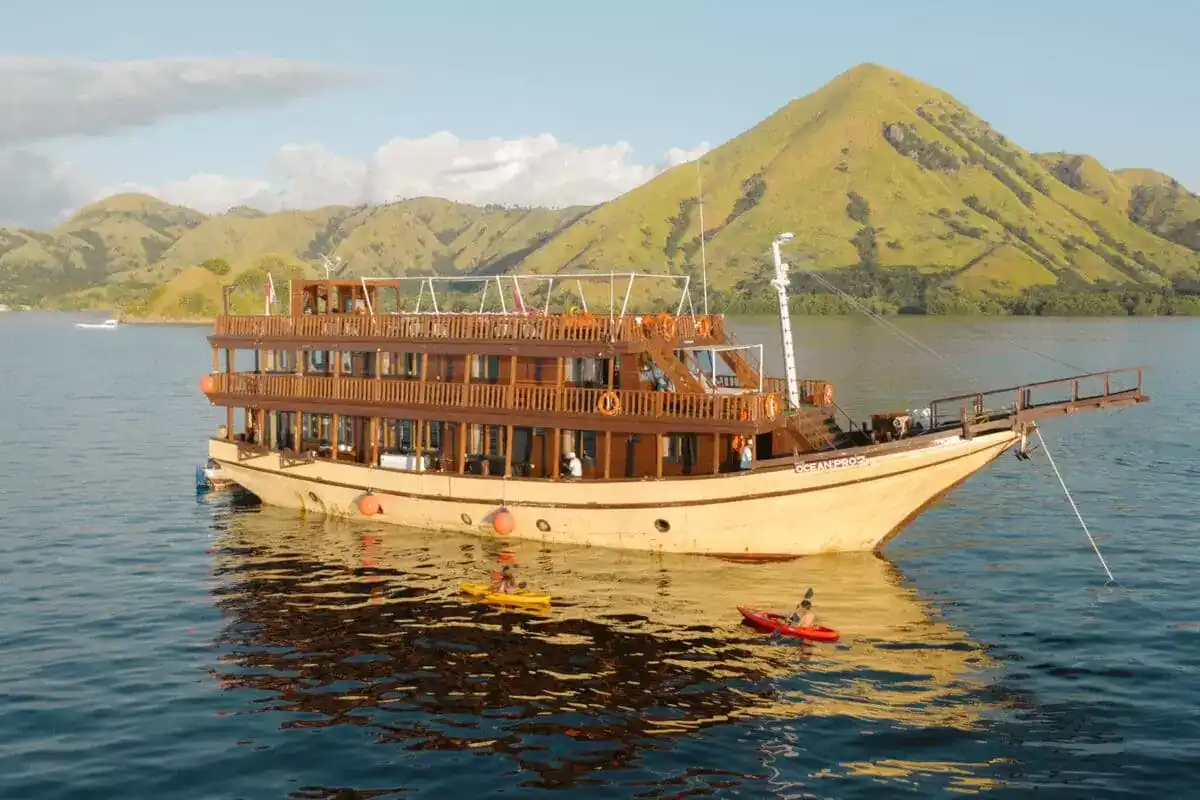 A phinisi at anchor in calm water with kayakers alongside